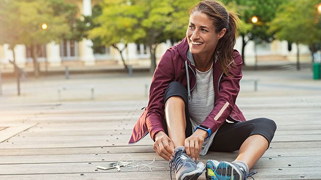 Frau in Sportkleidung sitzt drauÃen auf Holzplanken und bindet ihre Laufschuhe â sie lÃ¤chelt und wirkt bereit zum Joggen. (c) Ground Picture/Shutterstock.com