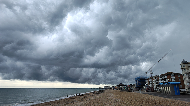 Thick, stormy clouds cover the sky at the coast. The sea is to the left with a beach taking centre frame.