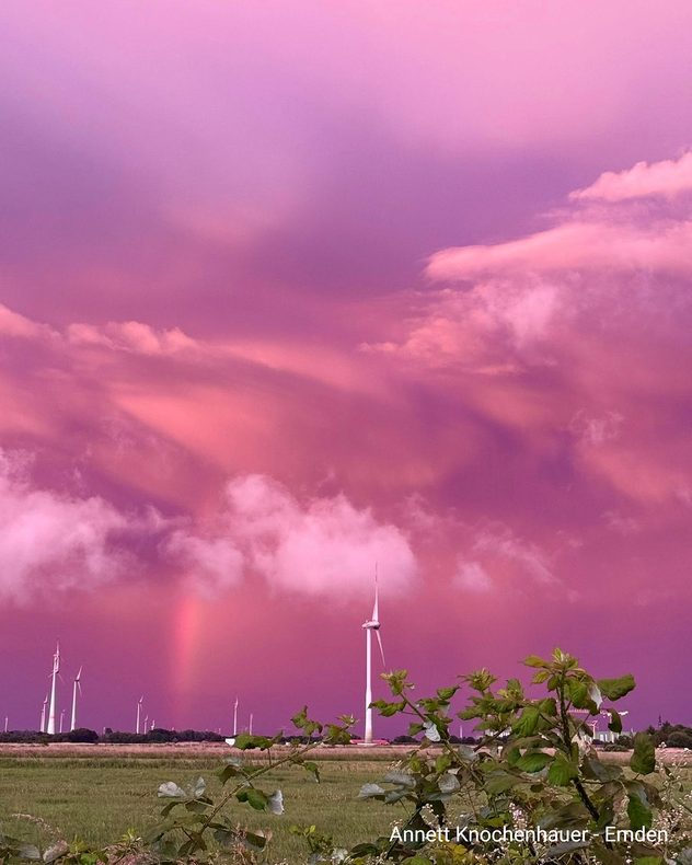 Landschaftsbild mit Windrädern und einem pinken Himmel inklusive Regenbogen