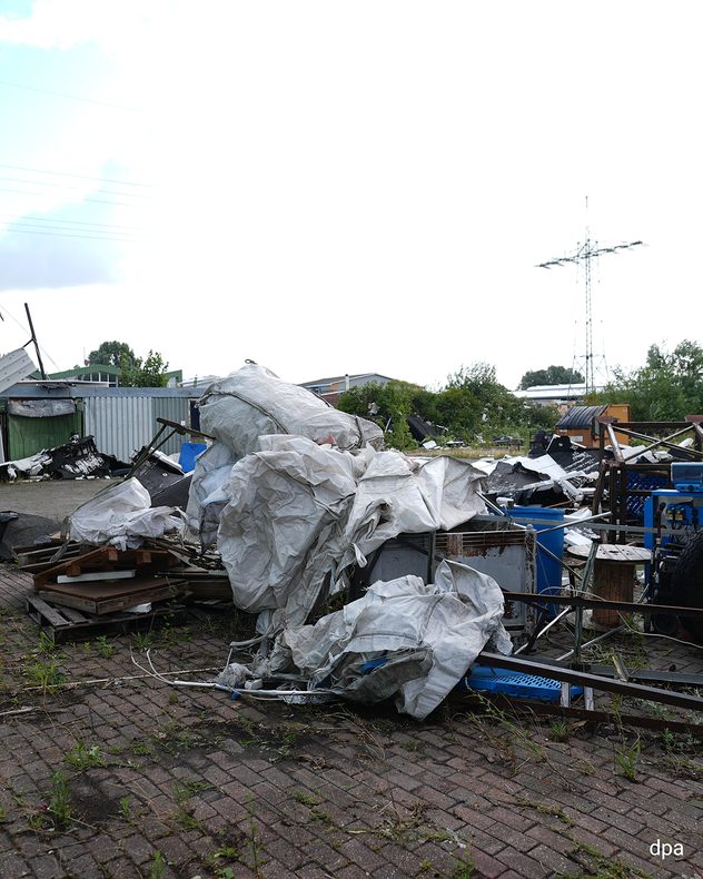 Große Dachelemente und Trümmer liegen nach einem Tornado auf dem Gelände einer Lagerhalle. Im Hintergrund sind weitere beschädigte Gebäude zu sehen.