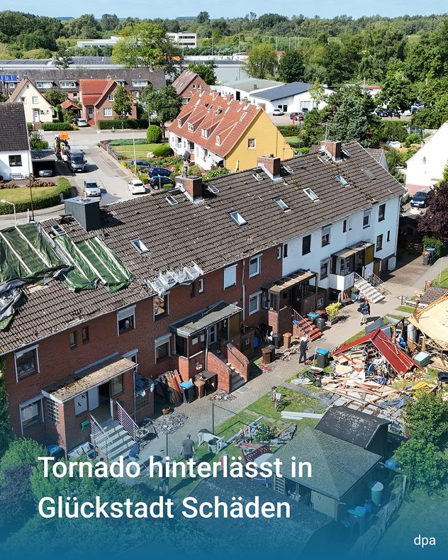 Drohnenaufnahme eines Wohngebiets mit beschädigten Reihenhäusern und zerstörten Gartenhäusern nach einem Tornado. Mehrere Dächer sind mit Planen gesichert, Trümmer liegen auf den Grundstücken.