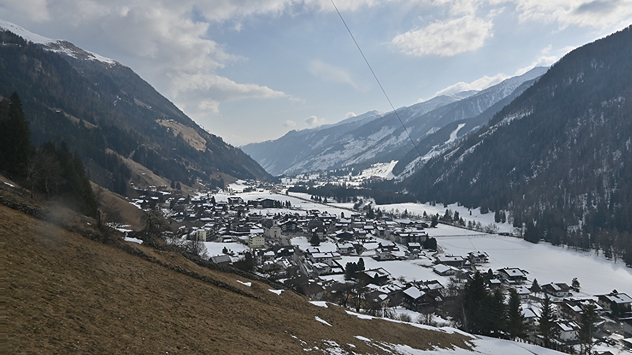 Das Webcambild zeigt ein Tal in den Alpen. Im Tal liegt noch Schnee, die Hänge sind hingegen grün.