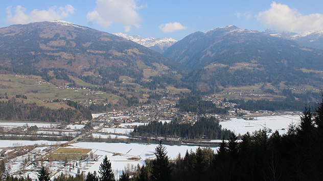 Das Webcambild zeigt ein Tal in den Alpen. Im Tal liegt noch Schnee, die Hänge sind hingegen grün.