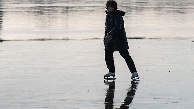  Auf den vom letzten Hochwasser überspülten Feldern haben sich Eisflächen gebildet. Eine Frau fährt darauf Schliitschuh 