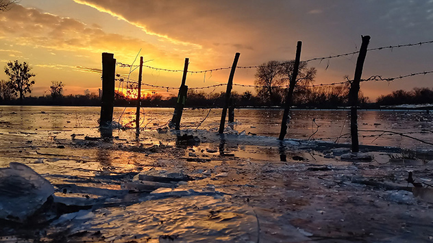 Das Abendrot spiegelt sich auf den gefrorenen Hochwasserflächen in Düsseldorf wieder.