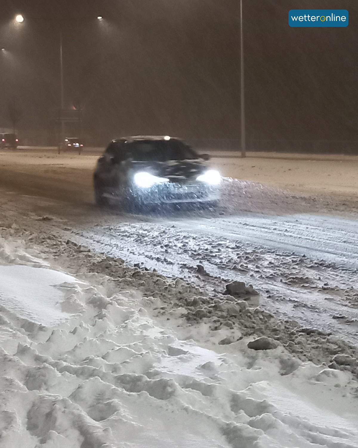 Car with lights on driving through deep slush on a winter road.