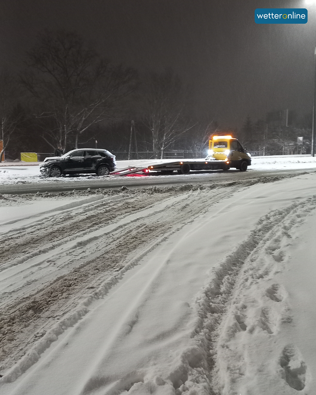 Tow truck loads a car on a snow-covered road at night.