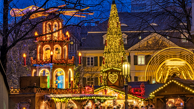 Bonner Weihnachtsmarkt bei Nacht mit hell erleuchtetem Weihnachtsbaum, Holzpyramide und festlich geschmückten Buden vor historischen Gebäuden.
