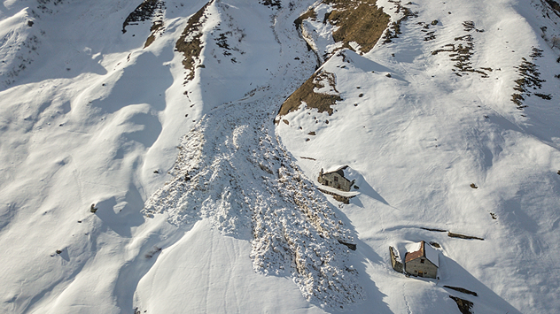Das Bild zeigt eine Lawine in den Bergen, die zwei Häuser nur knapp verfehlte.