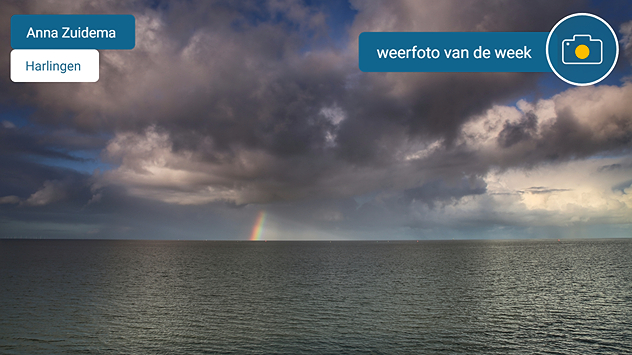 Een prachtige foto van de Waddenzee met een klein stukje regenboog zichtbaar onder een fraaie buienwolk.