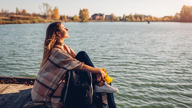 Eine Frau sitzt am Ufer eines Sees und genießt die Herbstsonne.