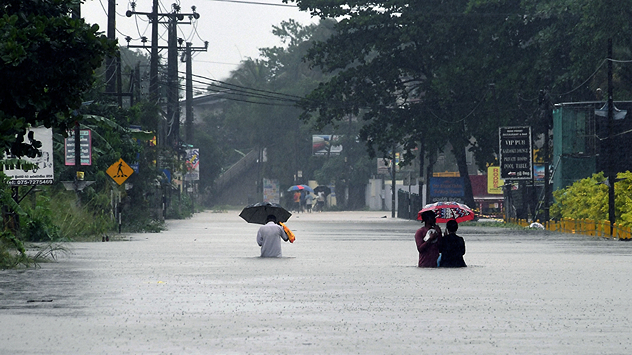 People wade through a heavily flooded street with umbrellas. Heavy rain makes visibility and movement difficult.