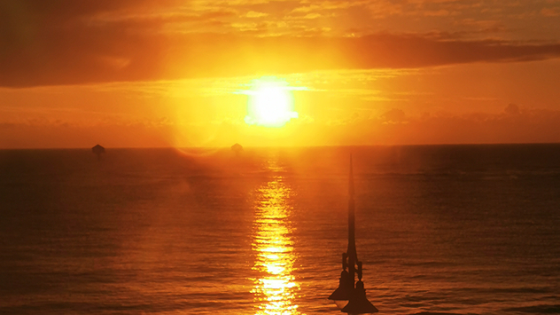 Bright orange sunrise over calm sea at Lowestoft, Suffolk, with sunlight reflecting on the water and a silhouetted structure in the foreground.