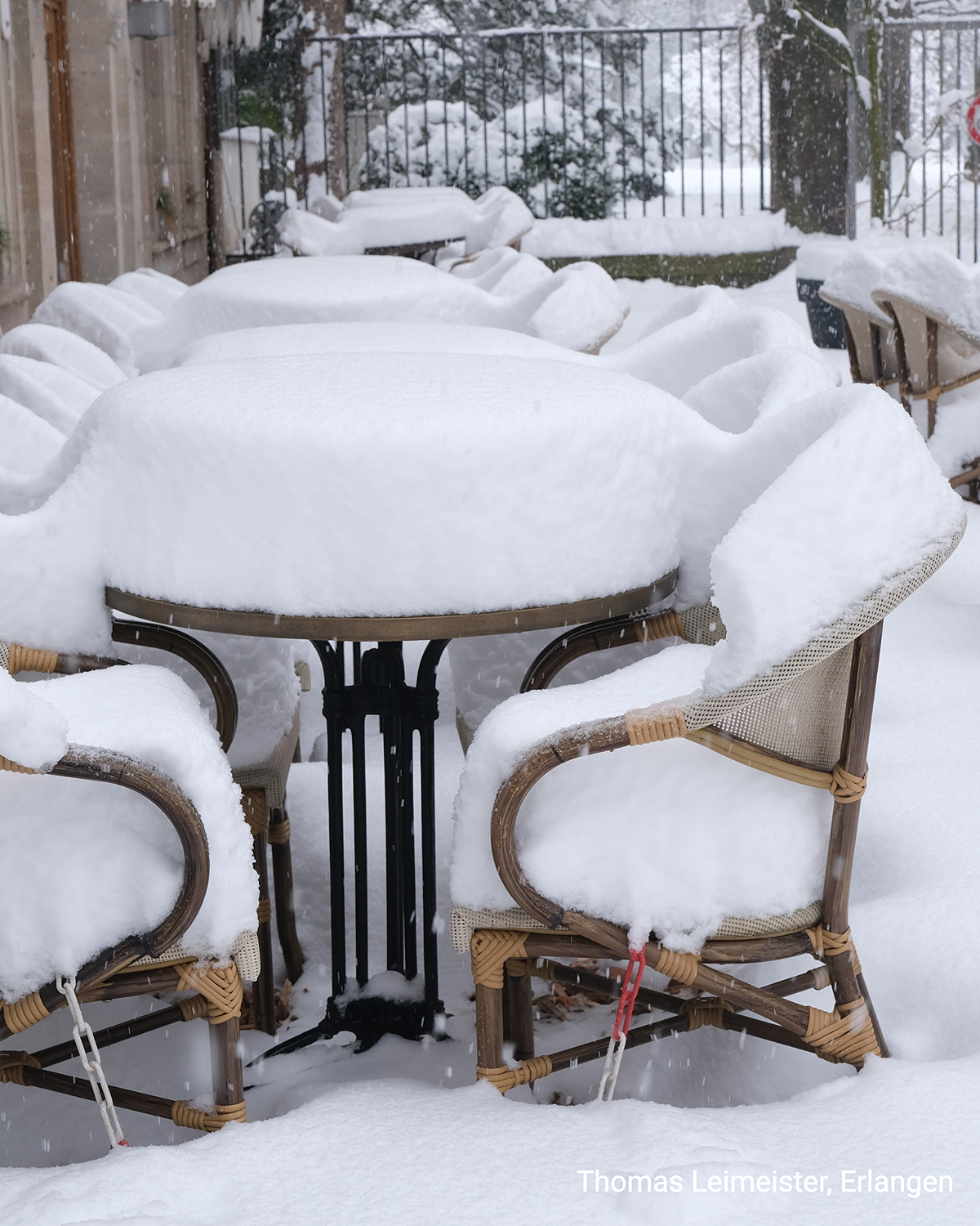Dicke Schneeschicht bedeckt Tisch und Stühle auf einer Terrasse. Während des Schneefalls ist kein Untergrund mehr sichtbar.