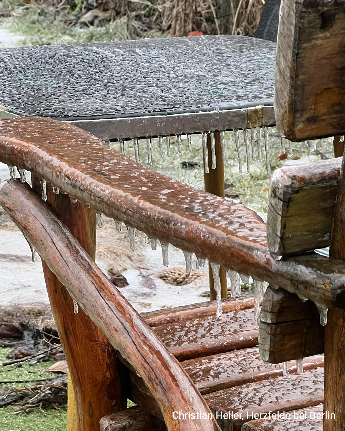 Eiszapfen hängen an einer Holzbank und einem Tisch nach gefrierendem Regen. Die Oberflächen sind glatt vereist.
