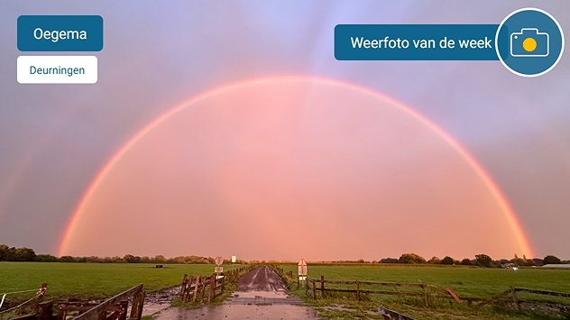 Een regenboog is in beeld gebracht. Door de lage zonstand kleuren de wolken onder de regenboog in fraaie kleuren.