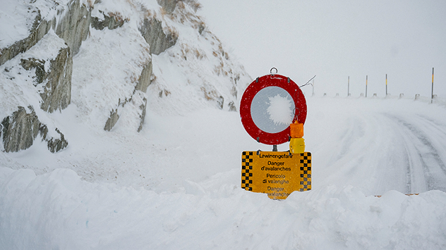 The picture shows a closed, snow-covered road. A sign warns of avalanche danger.