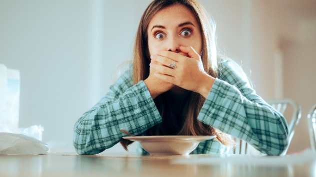 Frau am Tisch mit Suppenteller hält sich Hände an den Mund 