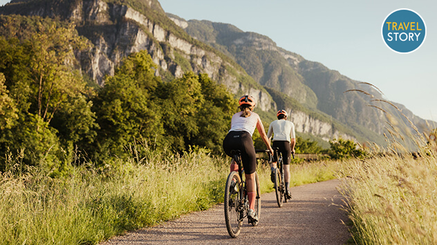 Zwei Radler unterwegs auf einem Fahrradweg, im Hintergrund Berge.