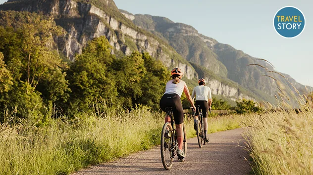 Zwei Radler unterwegs auf einem Fahrradweg, im Hintergrund Berge.