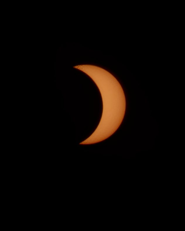 Orange crescent Sun during a partial solar eclipse against a black sky, with the Moon obscuring most of the solar disc.
