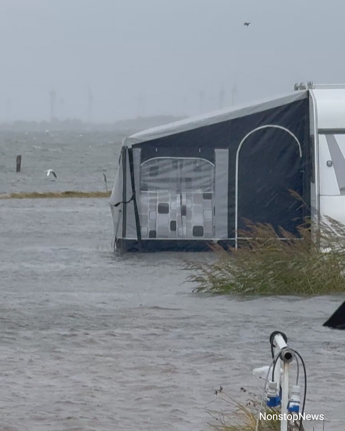 Überflutetes Vorzelt eines Wohnwagens auf einem Campingplatz bei starkem Regen und Wind, Wasser steht bis zum Zeltboden.