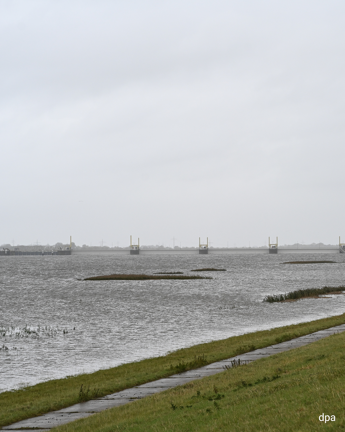 Emssperrwerk bei hohem Wasserstand unter grauem Himmel, Wasser reicht bis an den Deich.
