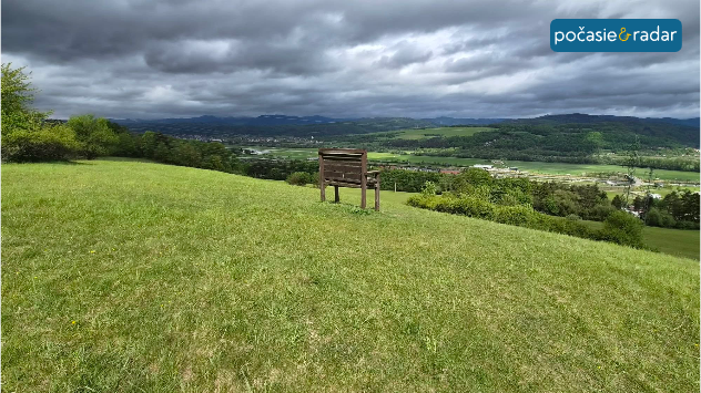 Tmavá oblačnosť nad zelenou krajinou, v pozadí údolie a kopce pred príchodom dažďa