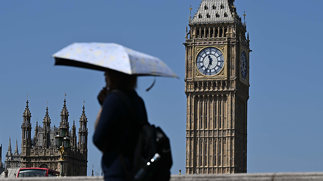 Person carrying a sun umbrella walking past the Elizabeth Tower in London under clear blue skies, using shade to cope with hot weather during a heatwave.