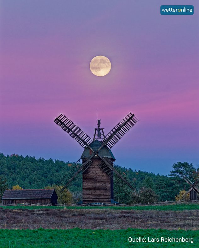 Vollmond über einer hölzernen Windmühle vor farbigem Abendhimmel.