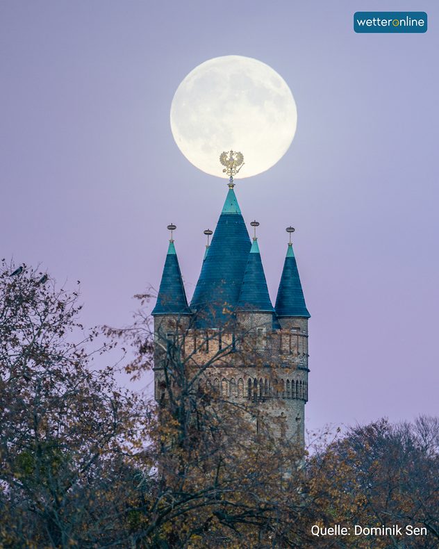 Vollmond über den Türmen eines alten Kirchturms bei violettem Himmel.