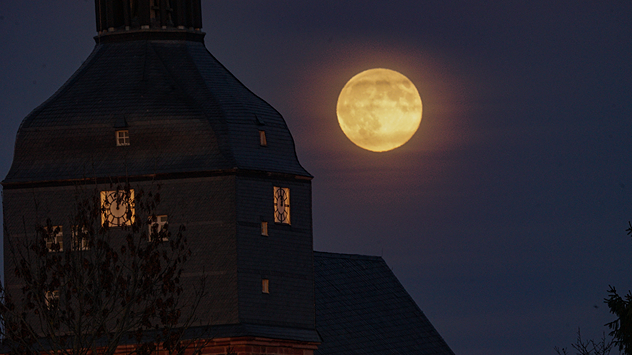 Vollmond über einem Kirchturm im dunklen Abendhimmel.