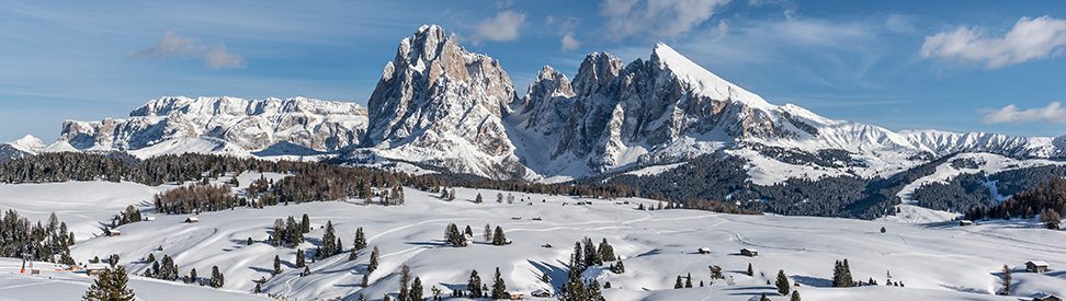 Verschneite Winterlandschaft auf der Seiser Alm mit Blick auf die markanten Dolomiten-Gipfel unter blauem Himmel. (c) Seiser Alm Marketing / Helmuth Rier