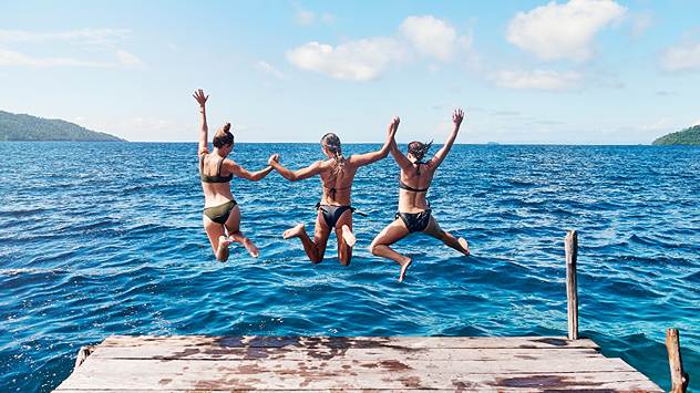 Drei Personen springen bei Sonnenschein in einen See