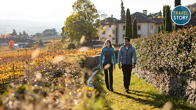 Ein Paar spaziert im Herbst durch Weinberge an der Südtiroler Weinstraße.