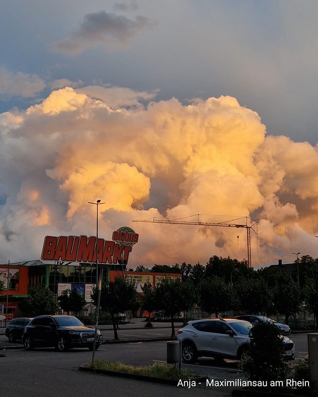 Große, goldgelb beleuchtete Gewitterwolke über einem Parkplatz und Gebäuden in Maximiliansau am Rhein.