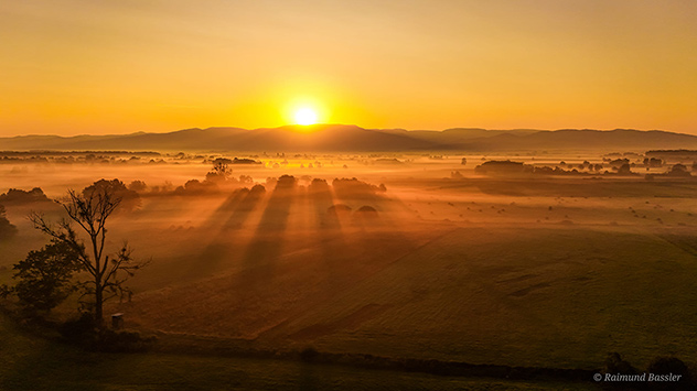 Felder im Nebel und darüber die aufgehende Sonne
