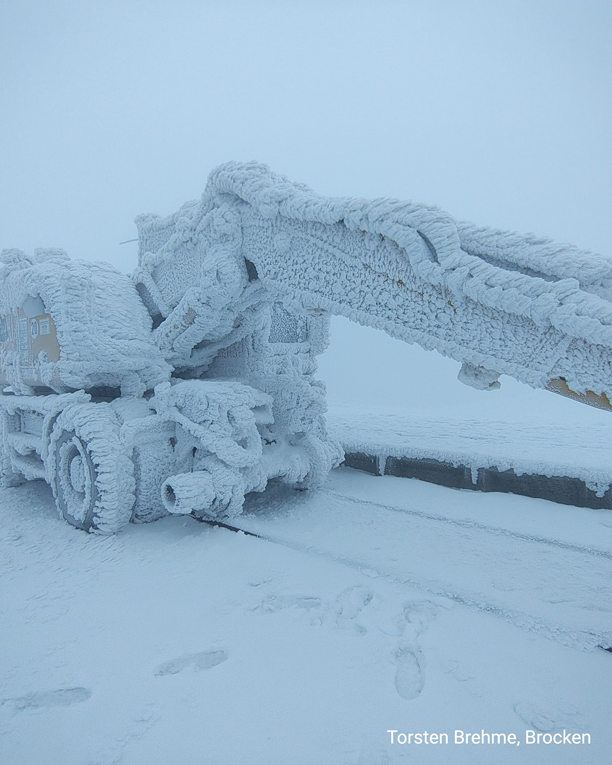 Vereister Kran auf dem Bagger, komplett mit Raureif überzogen. Dichter Nebel und Schnee prägen die winterliche Hochlagen-Szene.