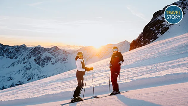 Zwei Skifahrer auf einer verschneiten Pisten bei Sonnenuntergang.