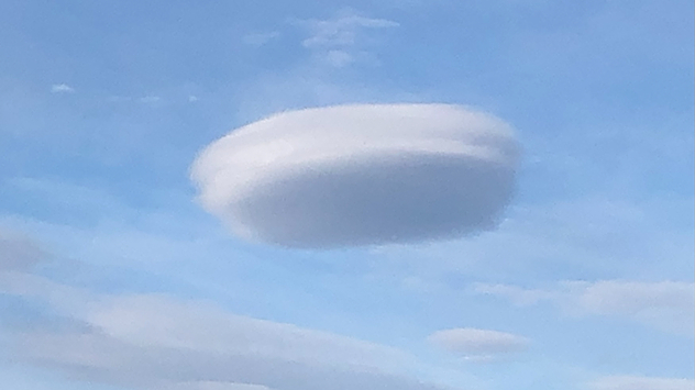 Linsenförmige Wolke (Lenticularis) am Himmel über Ruthin, Nordwales – sie erscheint glatt und elliptisch, fast wie ein UFO, vor blauem Himmel mit vereinzelten Wolken. Typisch für wellenförmige Luftbewegungen in der Nähe von Bergen.
