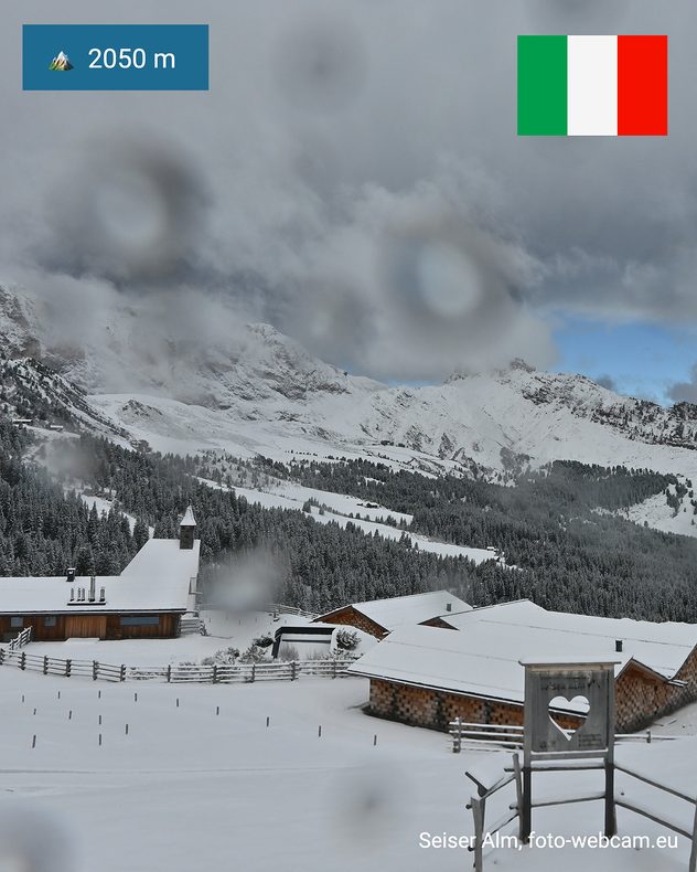 Paisaje nevado en la meseta de Seiser Alm, en Tirol del Sur, a 2050 metros de altitud. Tejados, bosques y montañas cubiertos de nieve bajo densas nubes.