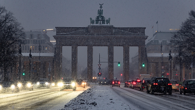 Verschneites Brandenburger Tor mit Straßenverkehr bei Schneefall in Berlin.