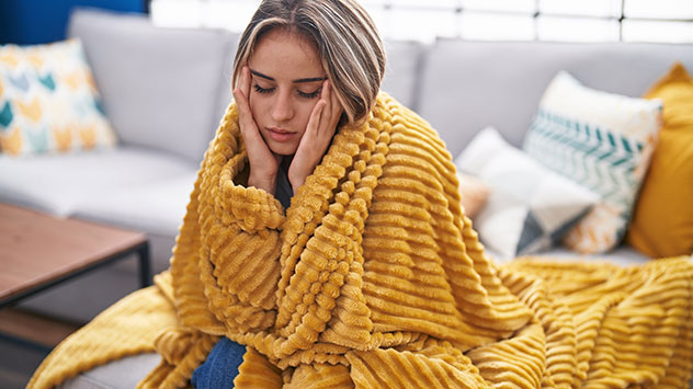 Eine Frau ist in eine Decke gehüllt und hat Kopfschmerzen.