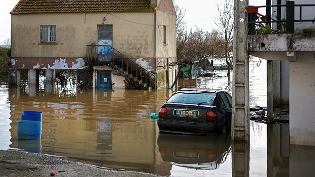 Затоплений житловий район з напівзатопленим автомобілем Вода стоїть між будинками та сходами.