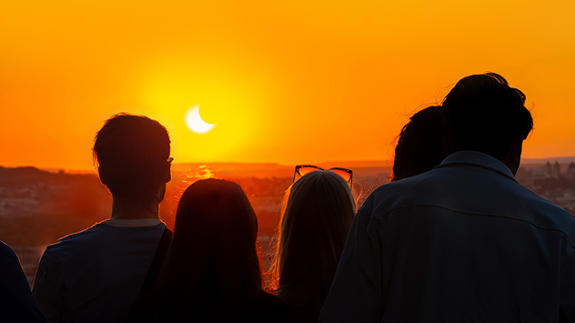 Des gens observent une éclipse solaire. Le soleil est déjà partiellement masqué.