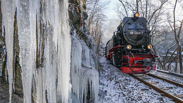 Die Brockenbahn fährt an großen Eiszapfen an einem Hang vorbei.