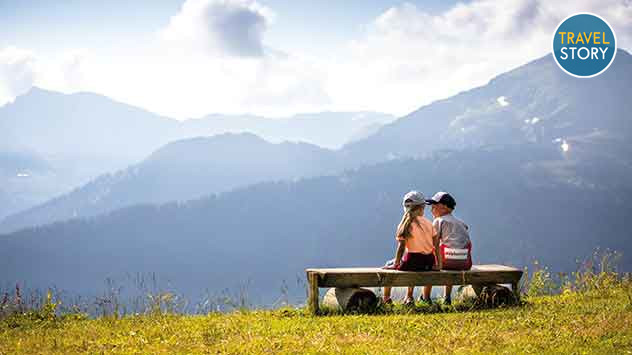 Zwei Kinder auf einer Bank mit Blick auf die Bergwelt. 