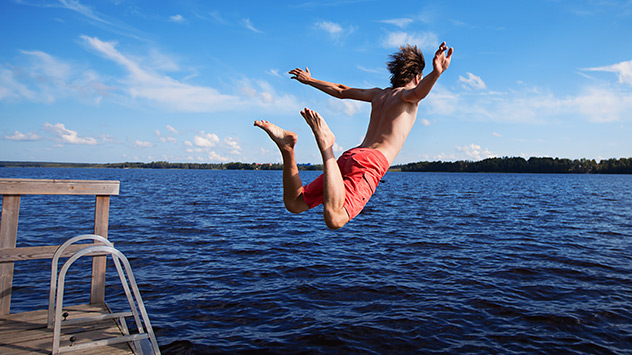 Ein Mann springt von einem Steg in einen See zum Baden