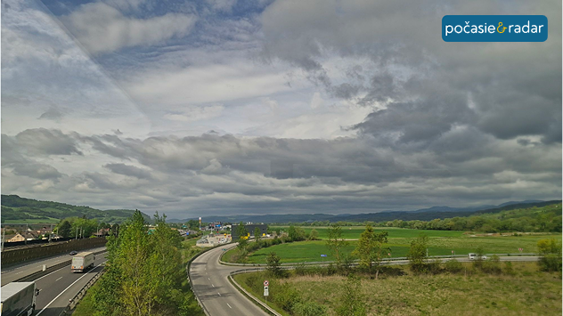 Zamračená obloha nad krajinou a cestou, v pozadí kopce a nízka oblačnosť