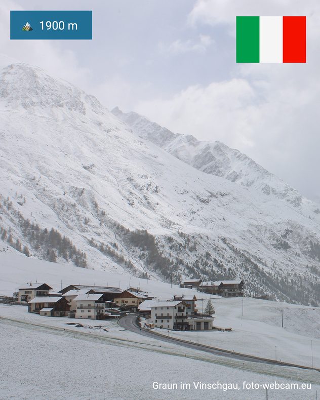 Paesaggio montano innevato nei pressi di Curon in Val Venosta, a 1900 metri di altitudine. Cime, pendii e case ricoperti di neve sotto un cielo densamente nuvoloso.